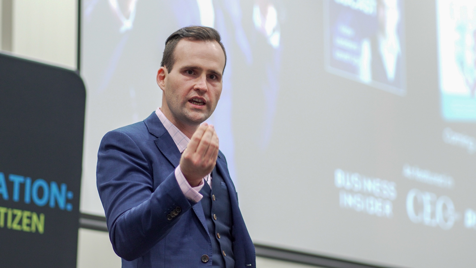 Andrew Ramsden speaking on stage in a suit, gesturing to the audience